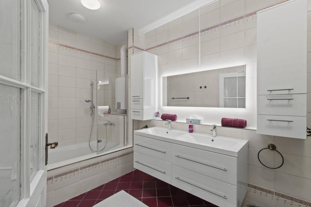 Modernes Badezimmer mit weißen Fliesen, Doppelwaschbecken, Badewanne mit Duschwand und roten Bodenfliesen.