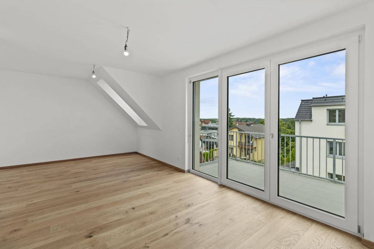 Heller Wohnraum mit Holzboden, Zugang zum Balkon und schrägen Wänden im Dachgeschoss.