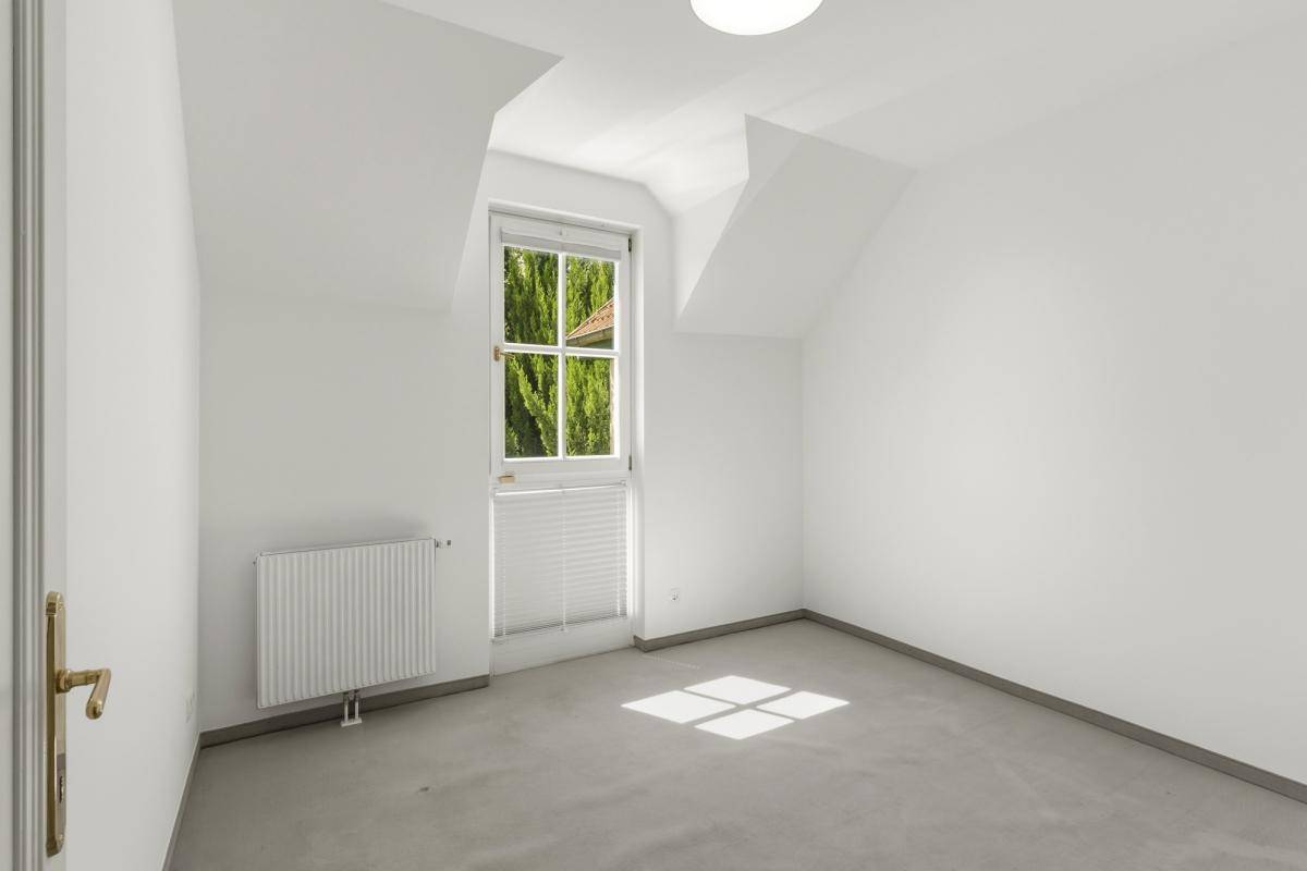Gemütliches Zimmer mit Teppichboden, schrägen Wänden und einem Fenster mit Jalousie.