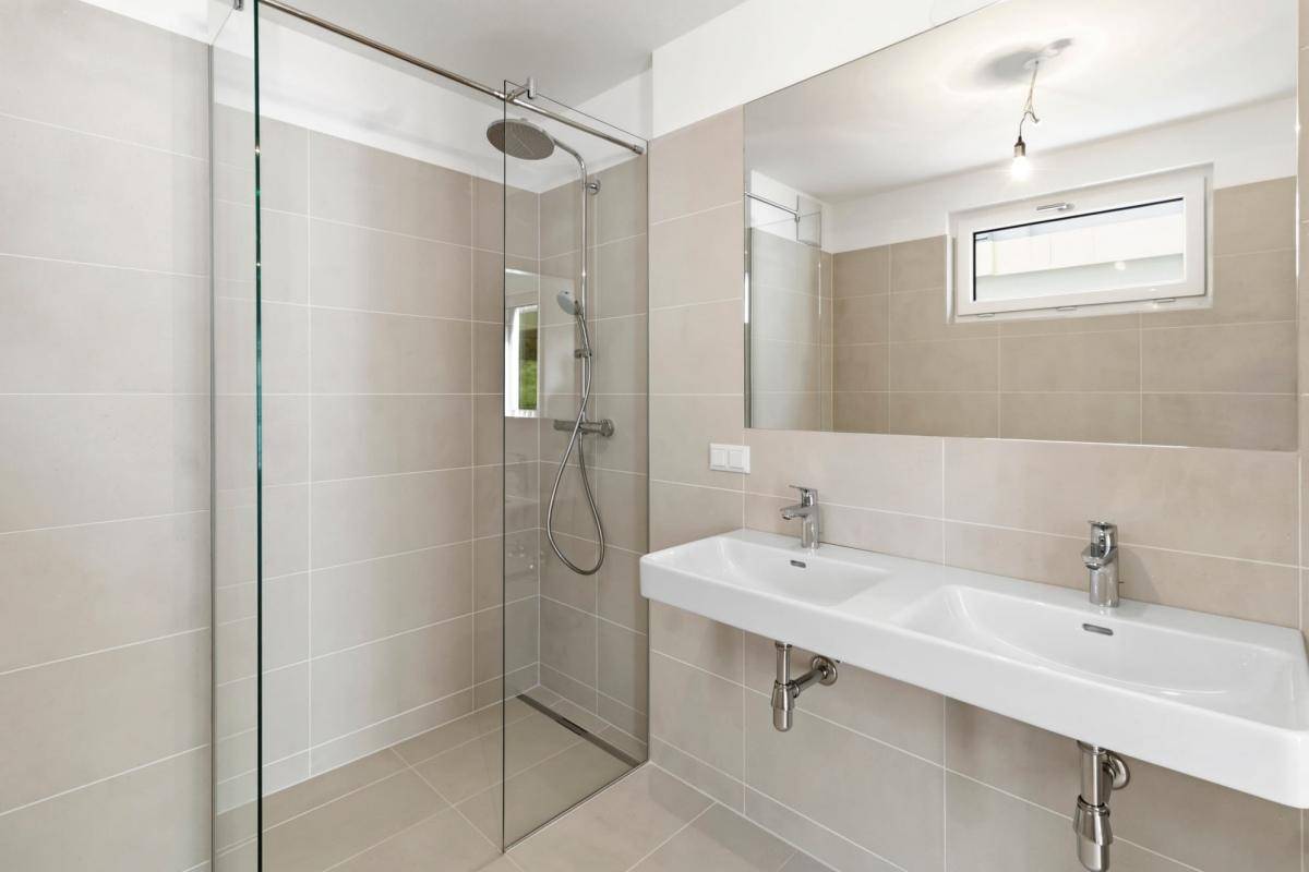 Modernes Badezimmer mit doppelten Waschbecken, großer Dusche und Fenster.