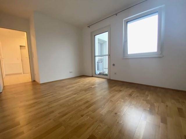 Helles Schlafzimmer mit Parkettboden, großem Fenster und Zugang zu einem Balkon oder einer Terrasse.