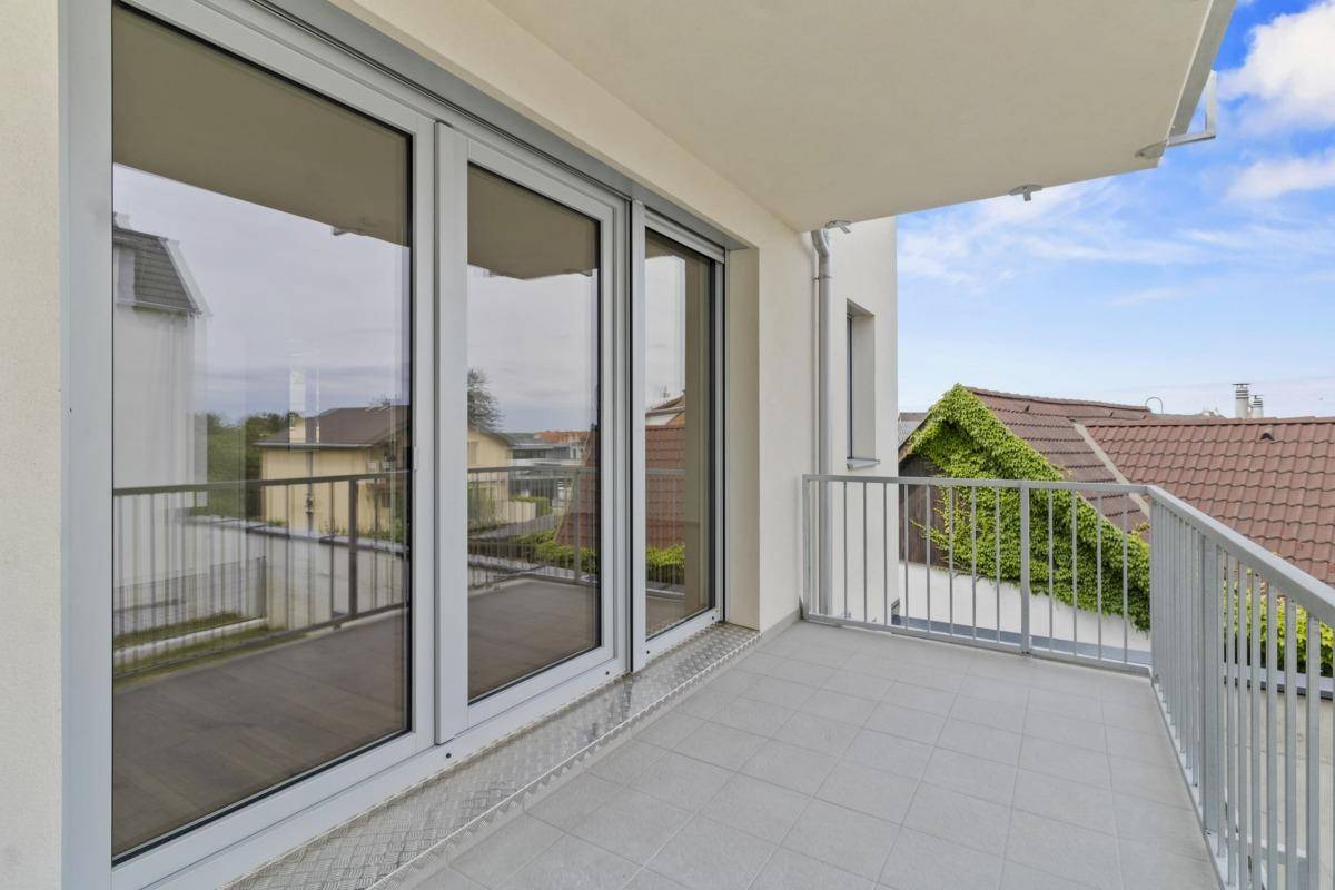 Heller Balkon mit Fliesenboden und großen Glasschiebetüren zum Innenbereich.