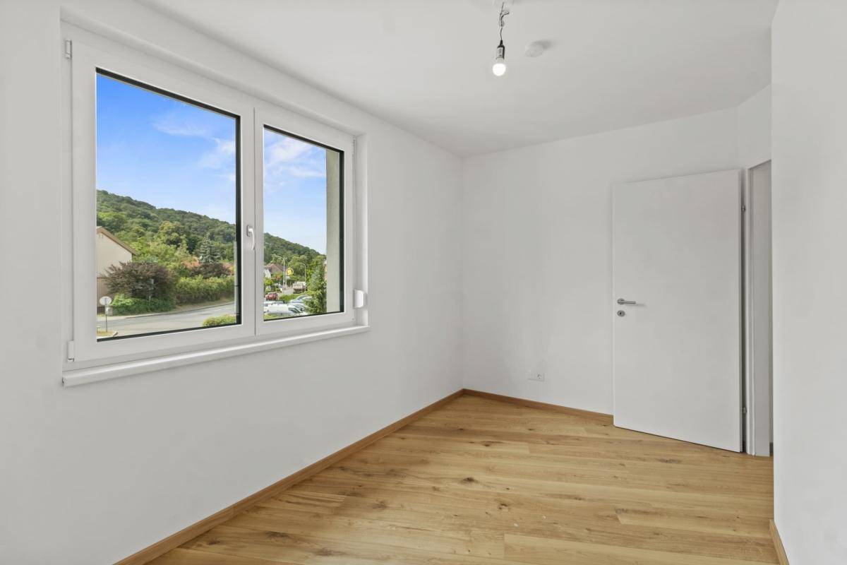 Helles Schlafzimmer mit Parkettboden und Fenster mit schöner Aussicht ins Grüne.
