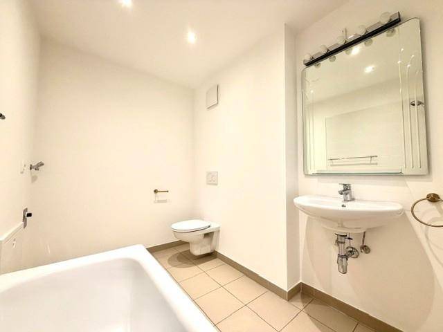 Helles Badezimmer mit Badewanne, wandhängendem WC und Spiegel über dem Waschbecken.