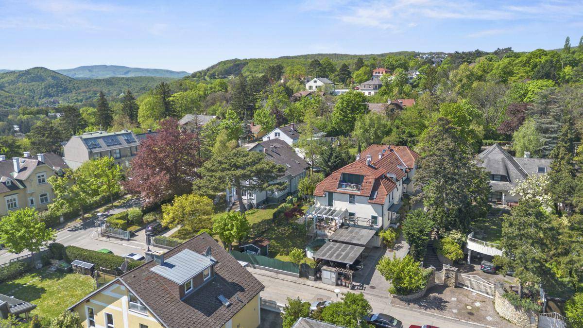 Luftaufnahme einer grünen Wohngegend mit vielen Bäumen und Häusern in hügeliger Landschaft.