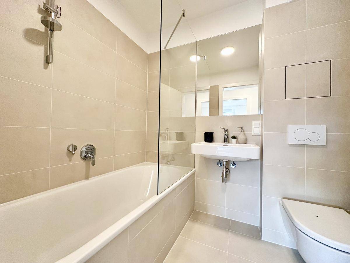 Modernes Badezimmer mit Badewanne, WC und Waschbecken, komplett in beigen Fliesen gehalten.