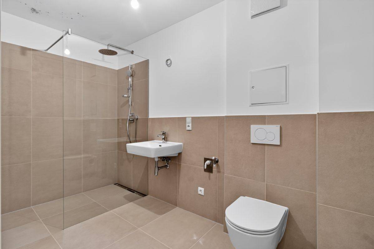 Helles Badezimmer mit begehbarer Dusche, Waschbecken und WC, gefliest in neutralen Tönen.
