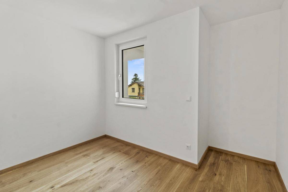 Schlafzimmer mit hellem Parkettboden und Fenster mit Blick ins Grüne.