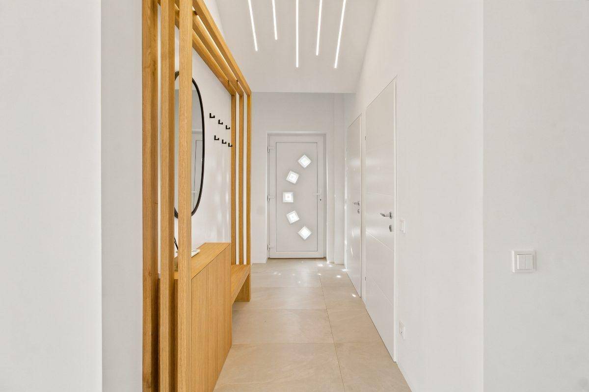 Heller Eingangsbereich mit Fliesenboden, Holzgarderobe und moderner Deckenbeleuchtung.