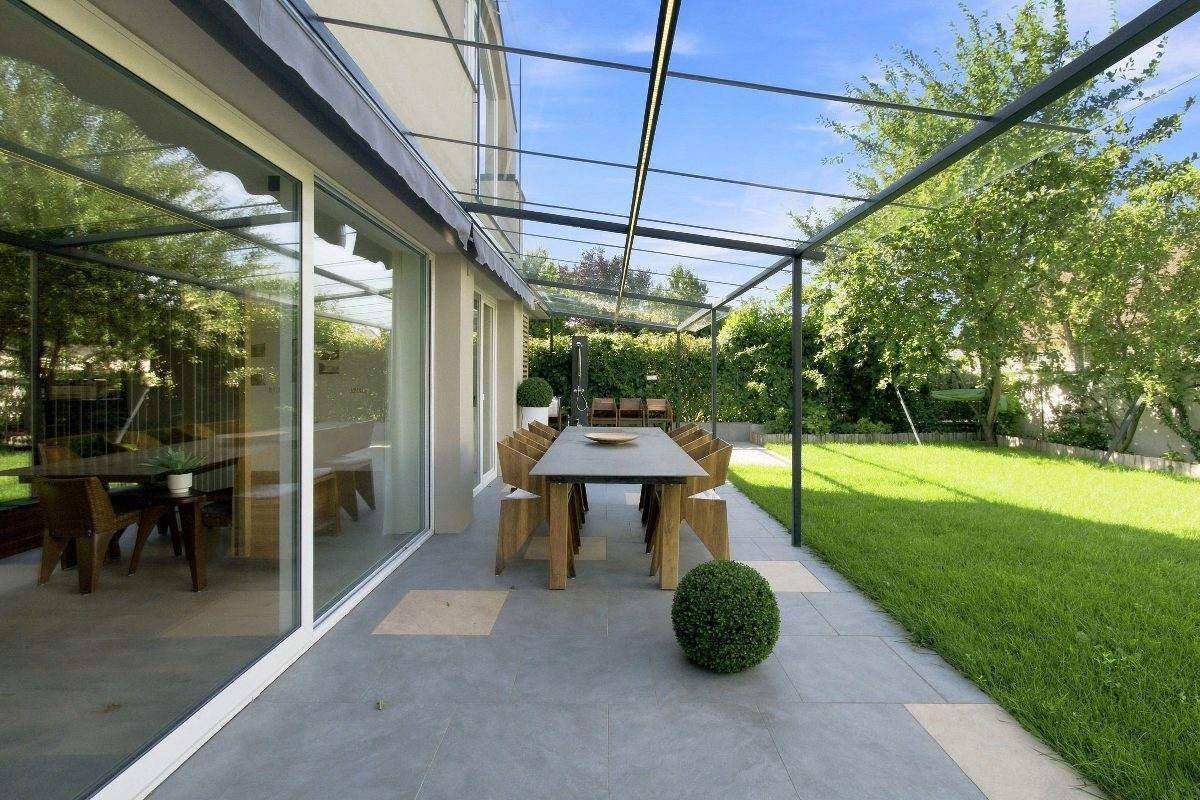 Große gepflasterte Terrasse mit Esstisch und Stühlen, umgeben von Grünflächen.