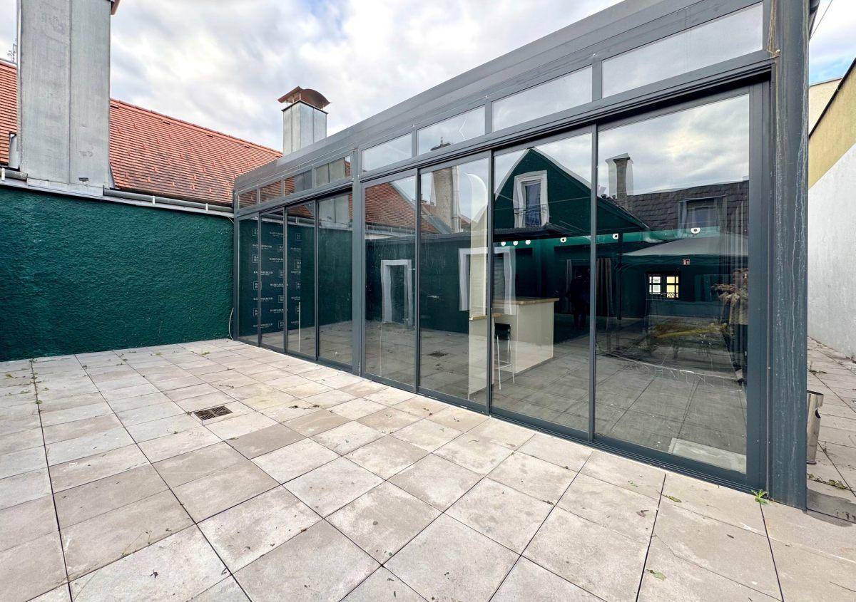 Gepflasterte Terrasse neben einem modernen Anbau mit großen Glasfronten und Blick in den Hof.