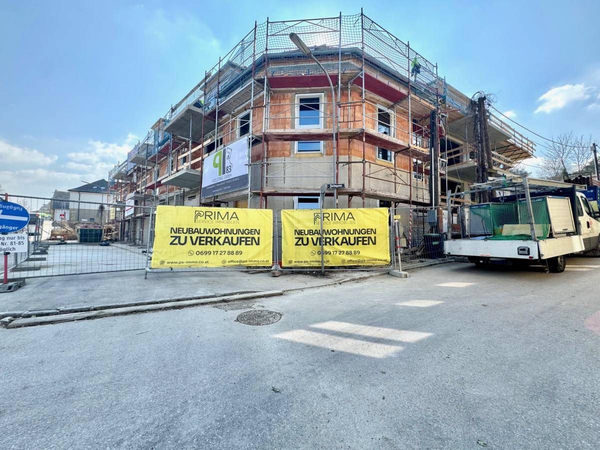 Eckansicht der Baustelle des Neubaus mit Gerüst und Werbebannern für Wohnungen.