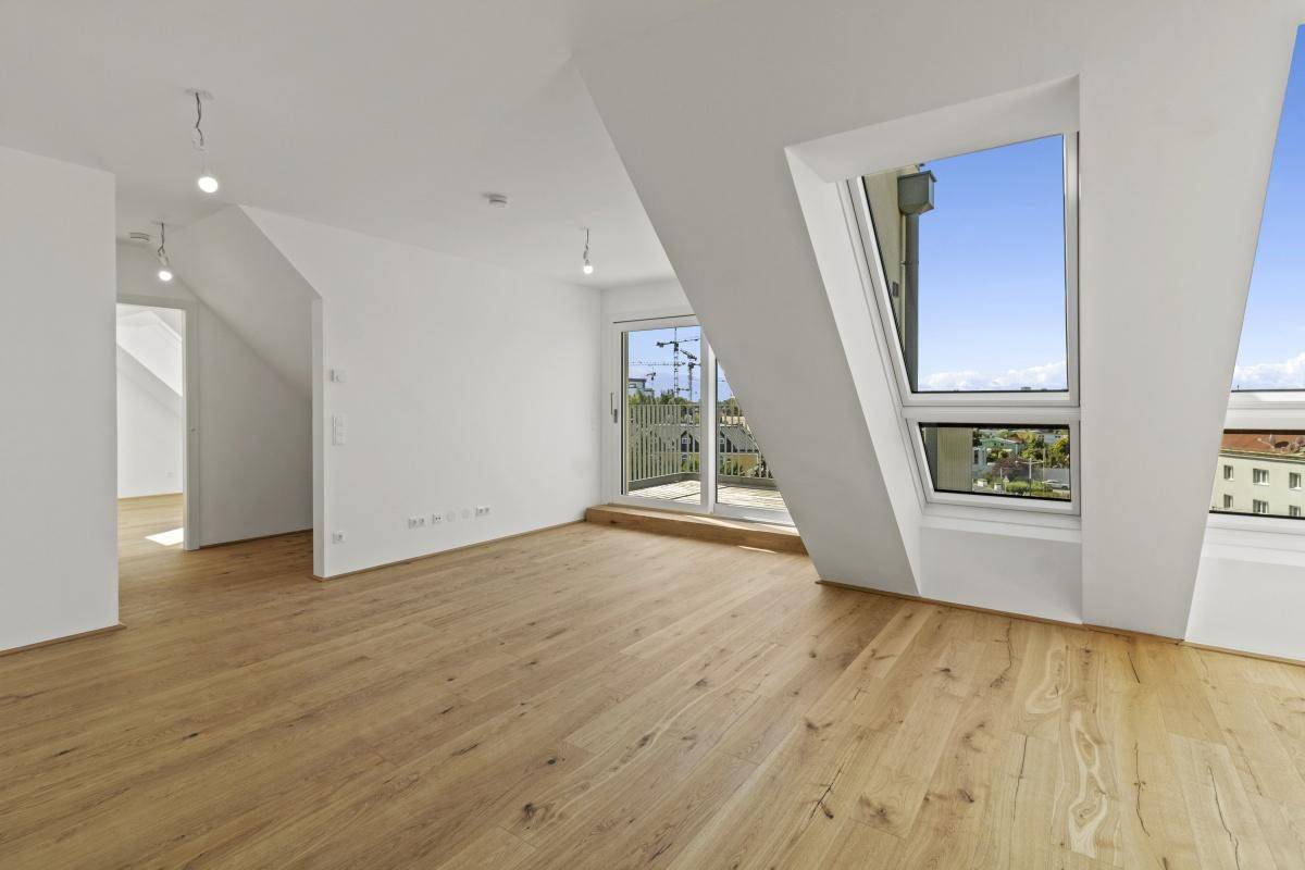 Lichtdurchfluteter Dachgeschossraum mit Holzboden, Balkonzugang und Blick über die Stadt.