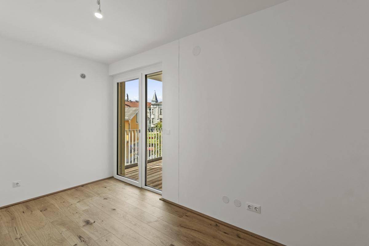 Helles Schlafzimmer mit Parkettboden und Zugang zu einem kleinen Balkon mit Stadtblick.