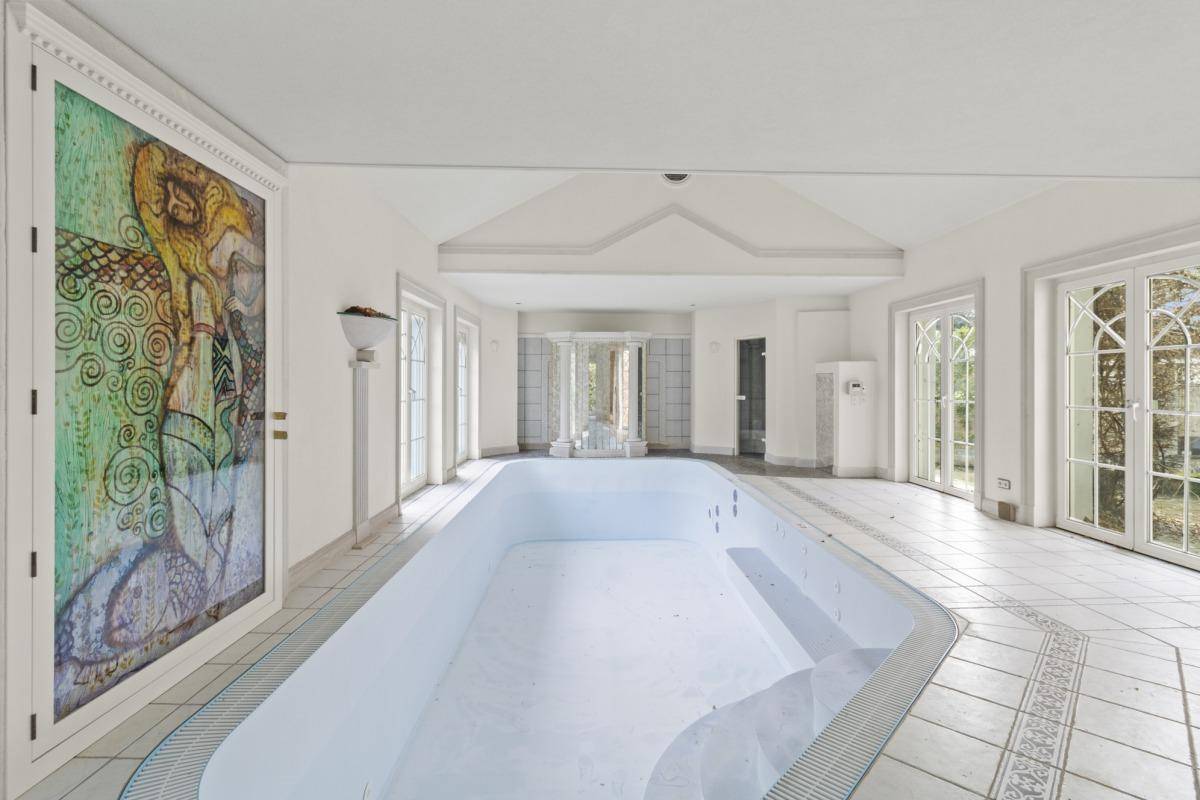 Heller Innenpoolraum mit kunstvoller Tür, hohen Decken und Blick in den Garten durch große Fenster.