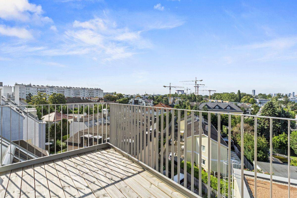 Großer Balkon mit Holzboden und Panoramablick auf die Stadt und Kräne am Horizont.