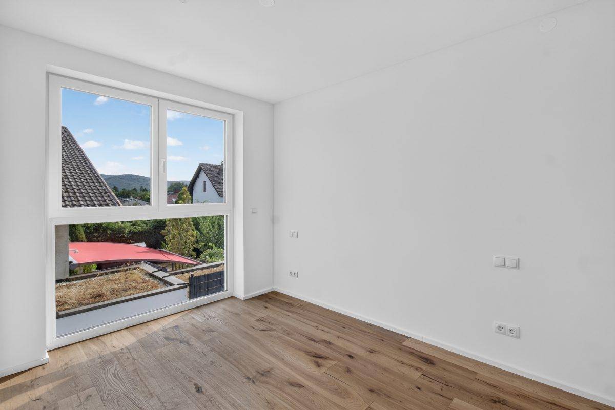 Helles Zimmer mit Holzboden und großem Fenster mit Blick ins Grüne.