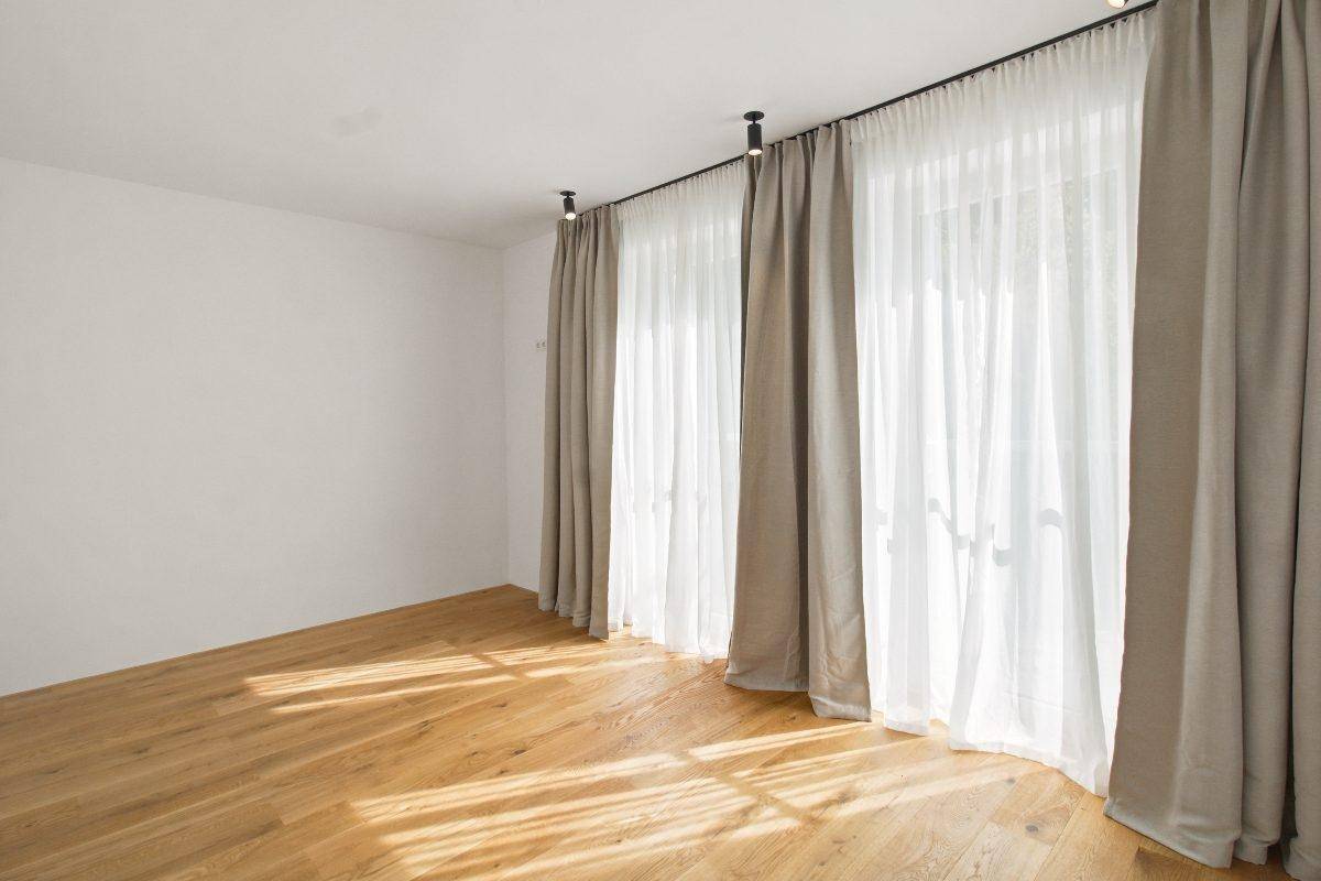 Leeres Zimmer mit Holzboden, großen Fenstern und viel natürlichem Tageslicht.
