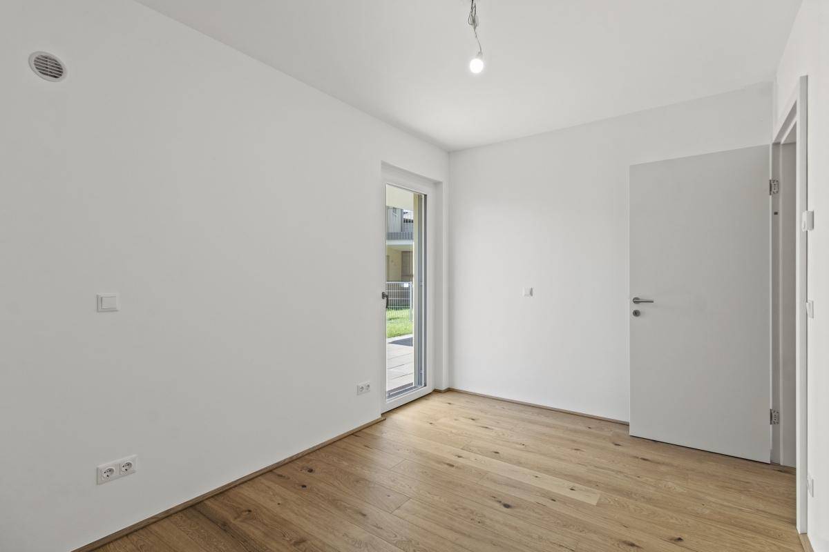 Geräumiges Zimmer mit Holzboden und Fenstertür, die auf eine Außenterrasse führt.