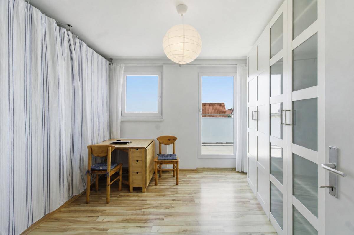 Helles Zimmer mit Holzboden, kleinem Schreibtisch und einem großen Kleiderschrank mit Milchglasfronten.