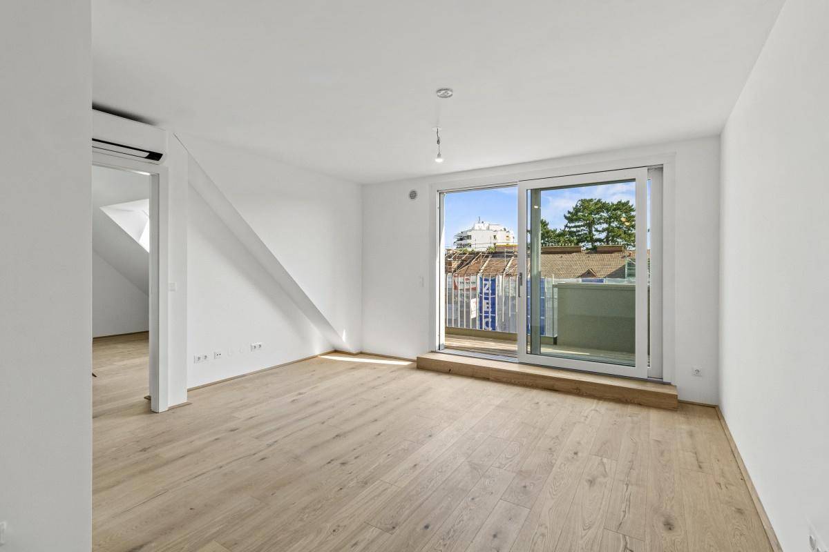 Lichtdurchfluteter Raum mit Holzboden, Zugang zum Balkon und schräger Decke.