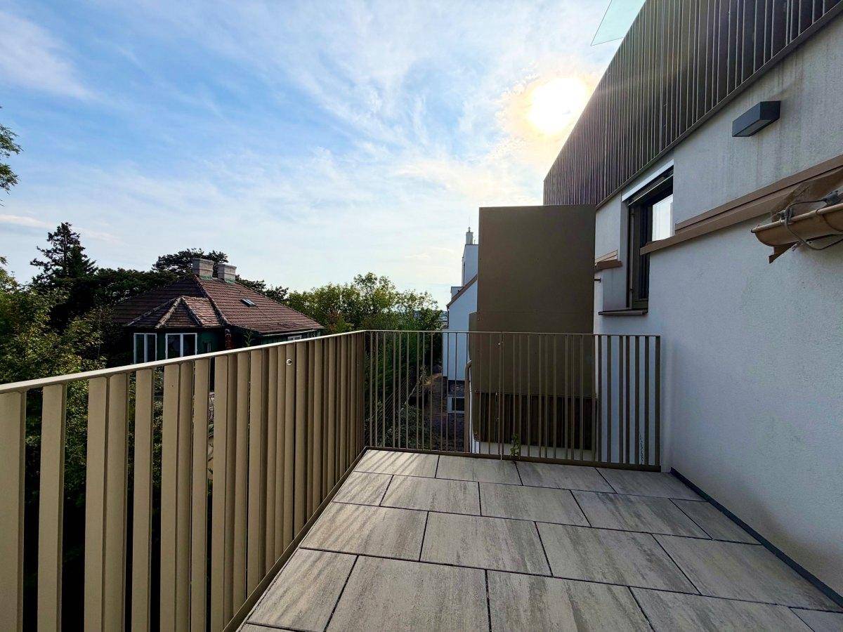 Sonniger Balkon mit Fliesenboden und modernem Geländer, umgeben von grüner Natur.