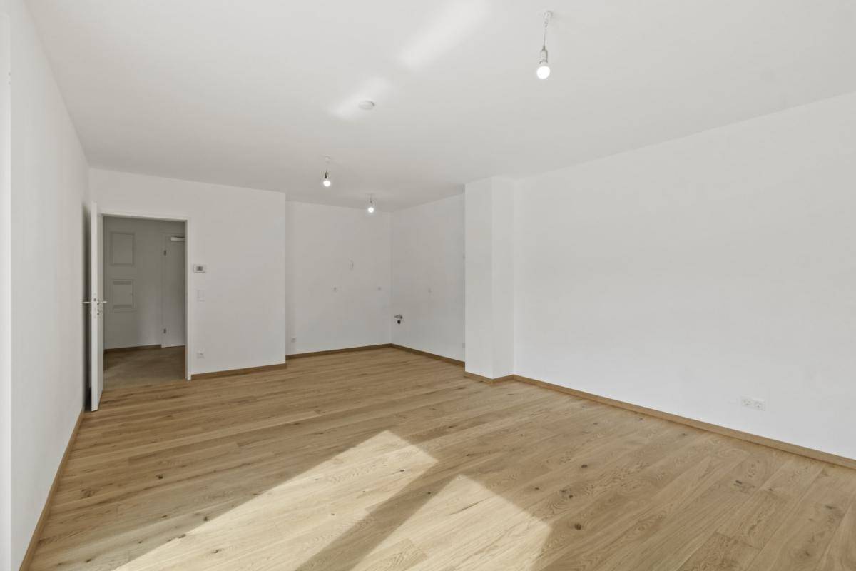 Leeres Wohnzimmer mit hellem Holzparkettboden und weißen Wänden, bereit zur Einrichtung.