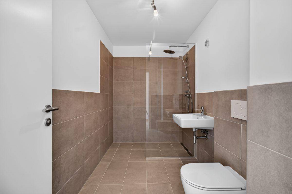 Modernes Badezimmer mit braunen Fliesen, Dusche und wandhängendem WC.