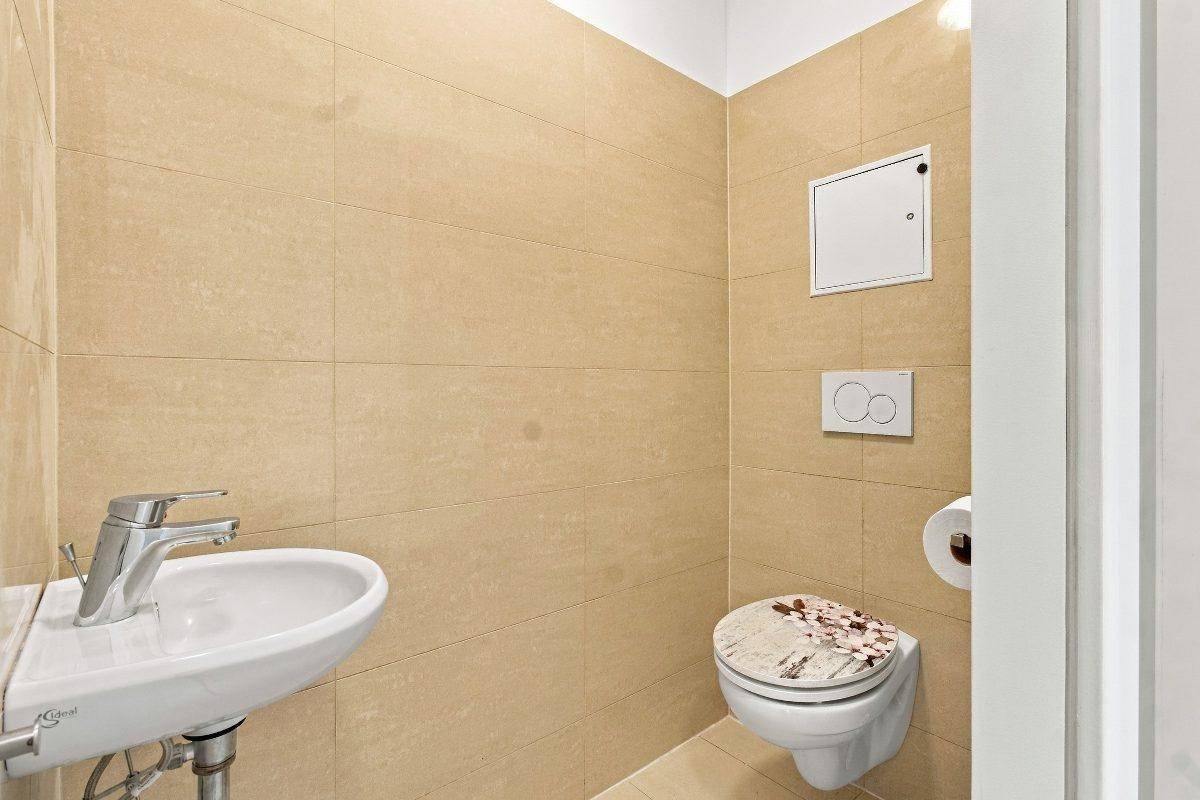 Modernes Gäste-WC mit beigen Fliesen, wandhängendem WC und kleinem Waschbecken.