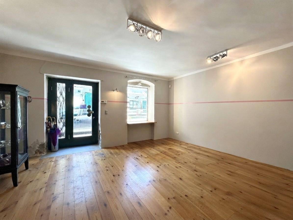 Geräumiger Geschäftsraum mit Holzdielenboden, hohen Decken und einer breiten Eingangstür, die viel Licht hereinlässt.