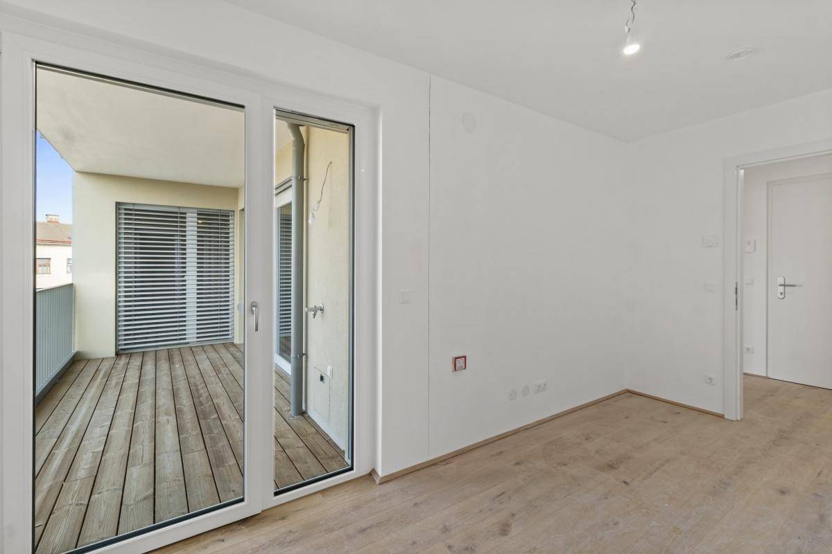 Heller Raum mit Holzboden und breiter Schiebetür zum Balkon.
