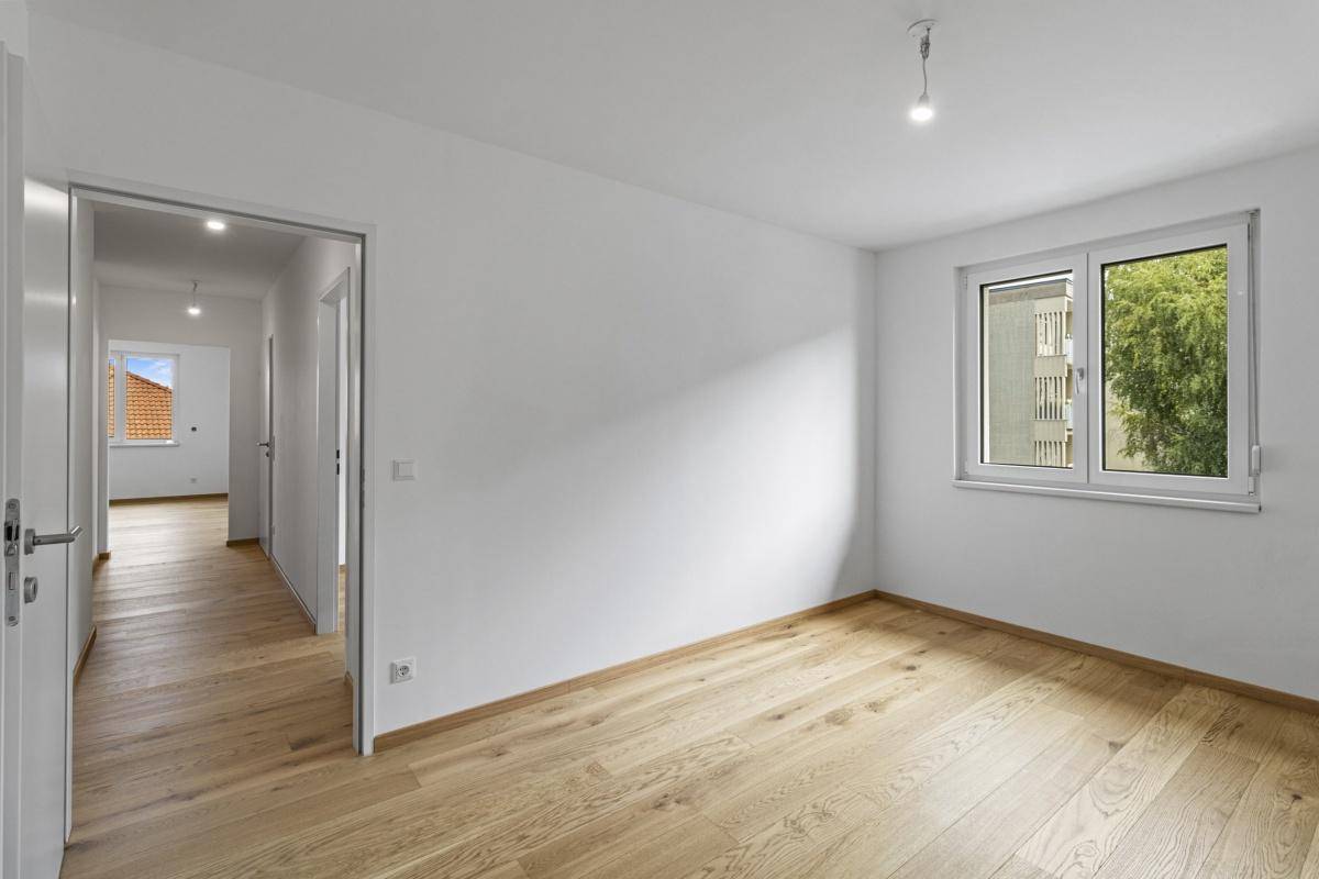 Helles Schlafzimmer mit Parkettboden und Zugang zu einem Flur, bereit zur Einrichtung.