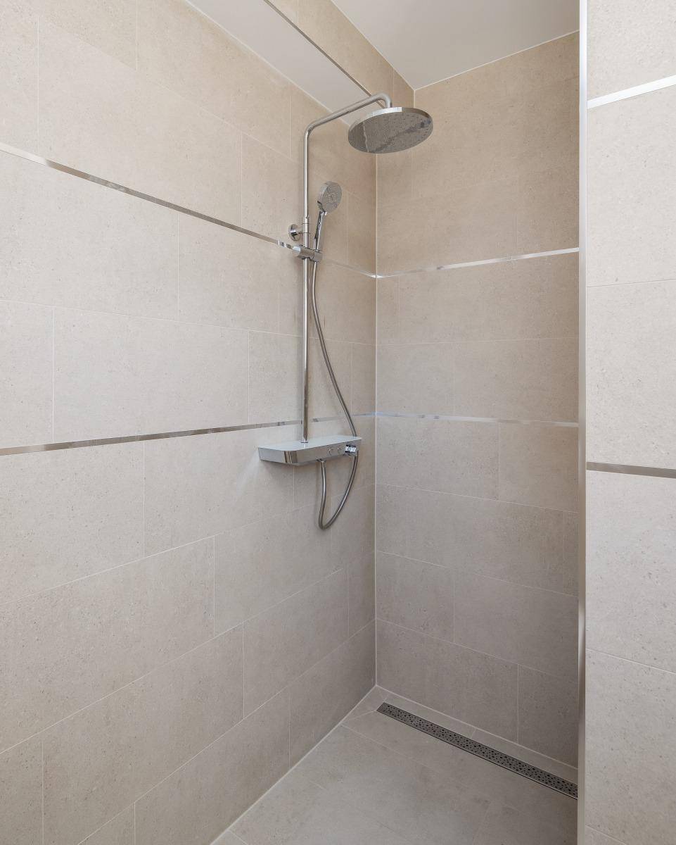 Geräumige, ebenerdige Dusche mit Regenduschkopf und modernen beigen Fliesen im Badezimmer.