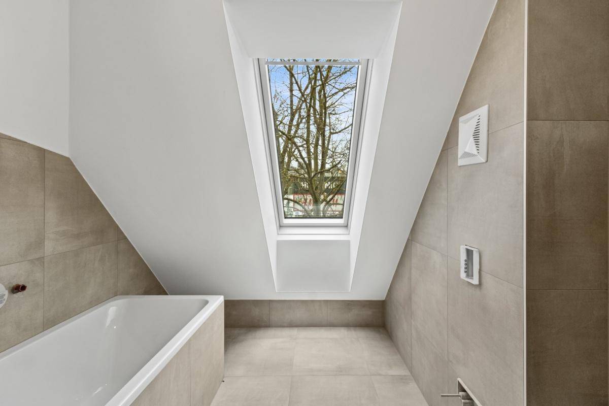 Modernes Badezimmer mit Badewanne, beigefarbenen Fliesen und einem Dachfenster für natürliches Licht.