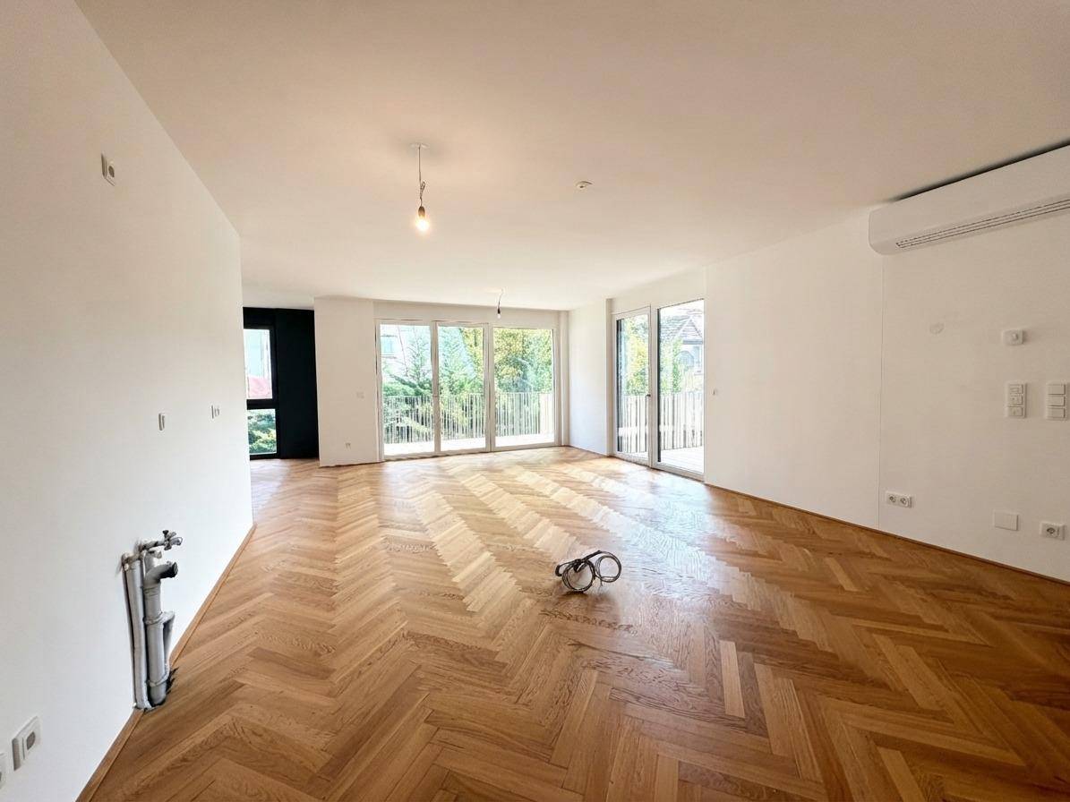 Helles Wohnzimmer mit Fischgrätparkett, großen Fenstern und Vorinstallationen für eine Küche oder Medienwand.