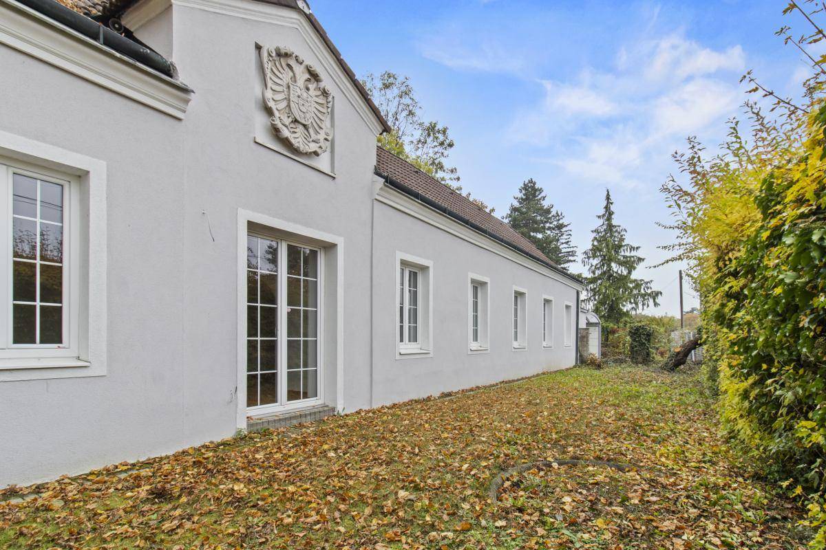 Seitenansicht eines historischen Gebäudes mit weißer Fassade, verzierten Fenstern und einem Wappen unter blauem Himmel.
