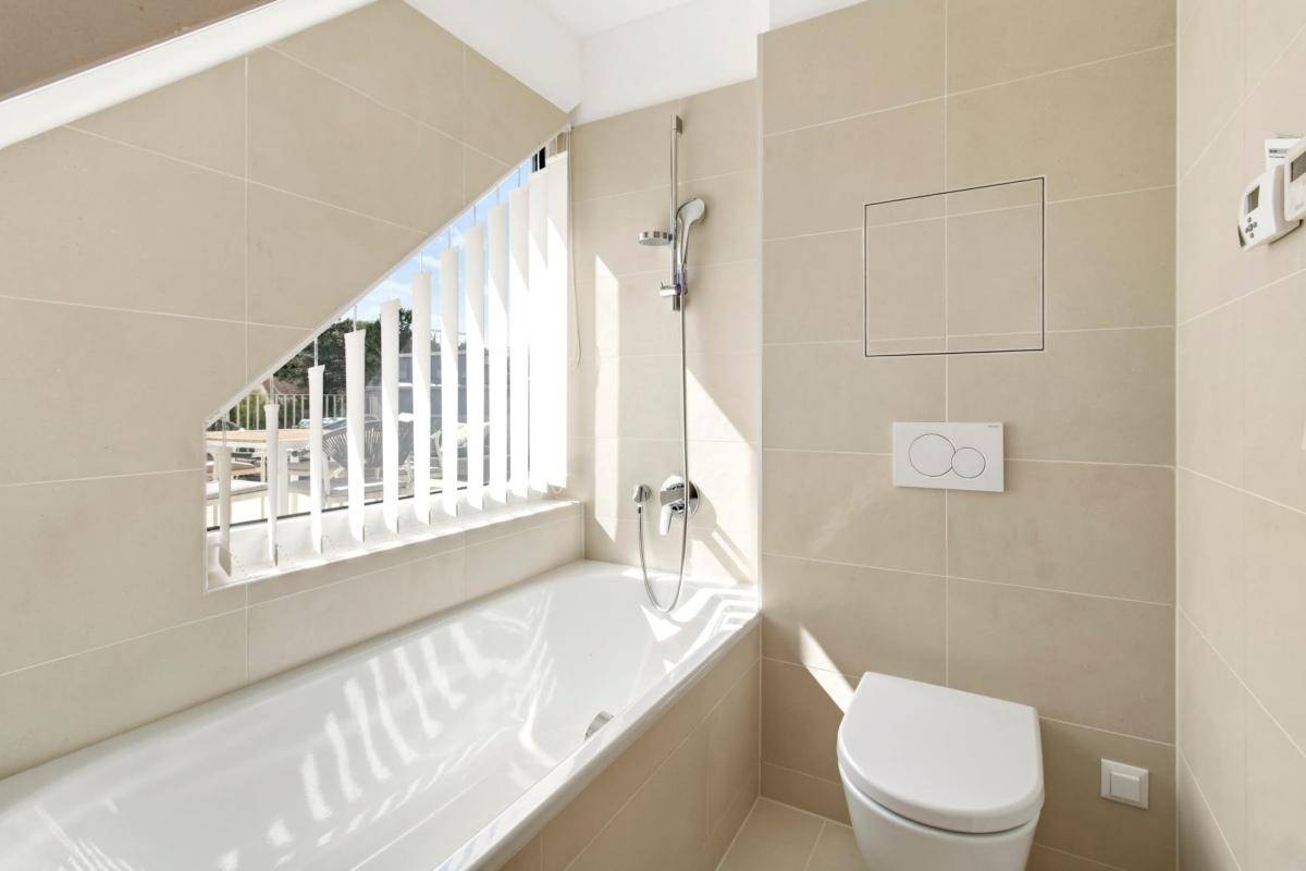Modernes Badezimmer mit Badewanne, Wand-WC und schrägen Fenstern.