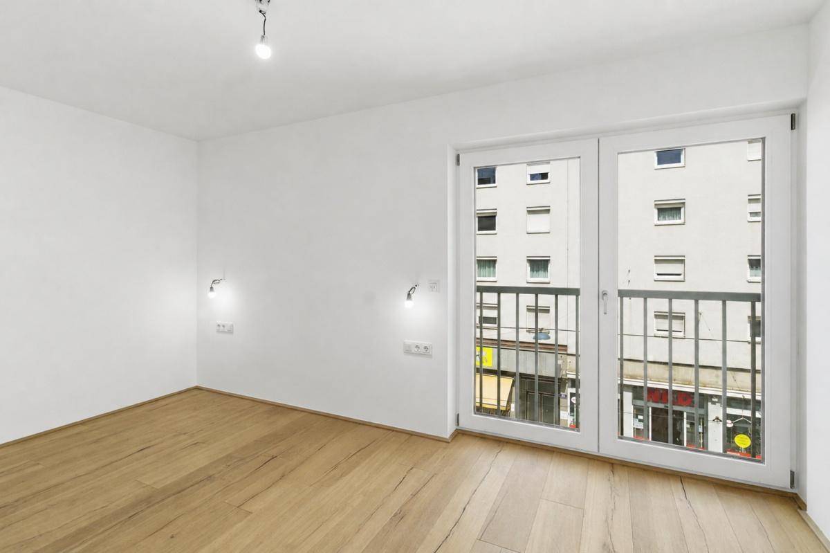 Heller Raum mit Holzfußboden und französischem Balkon, bietet einen Blick auf die Stadt.