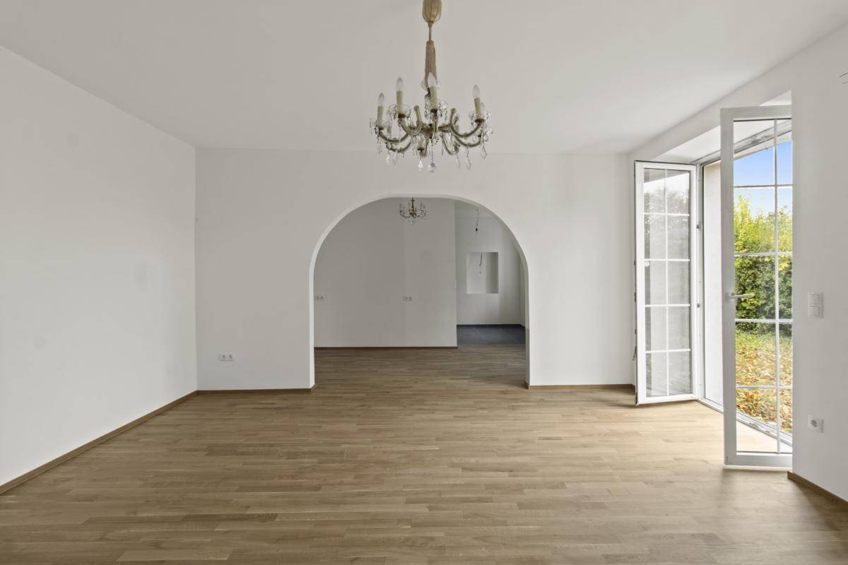 Geräumiges Wohnzimmer mit Holzboden, Rundbogen und Zugang zum Garten.