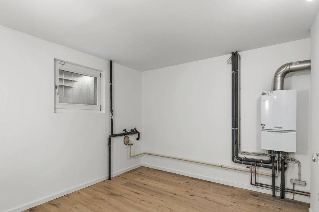 Hauswirtschaftsraum mit Heizungsanlage, sichtbaren Leitungen und kleinem Fenster.
