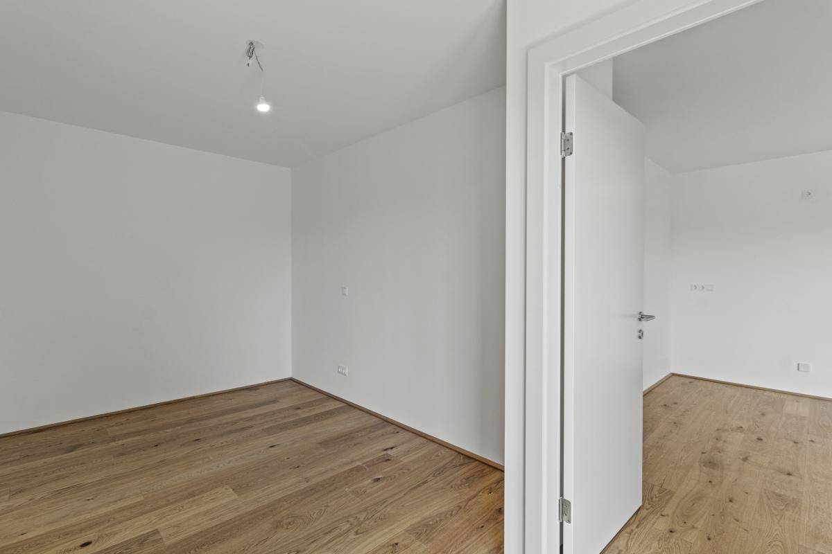 Leeres Schlafzimmer mit hellem Parkettboden und weiß gestrichenen Wänden.