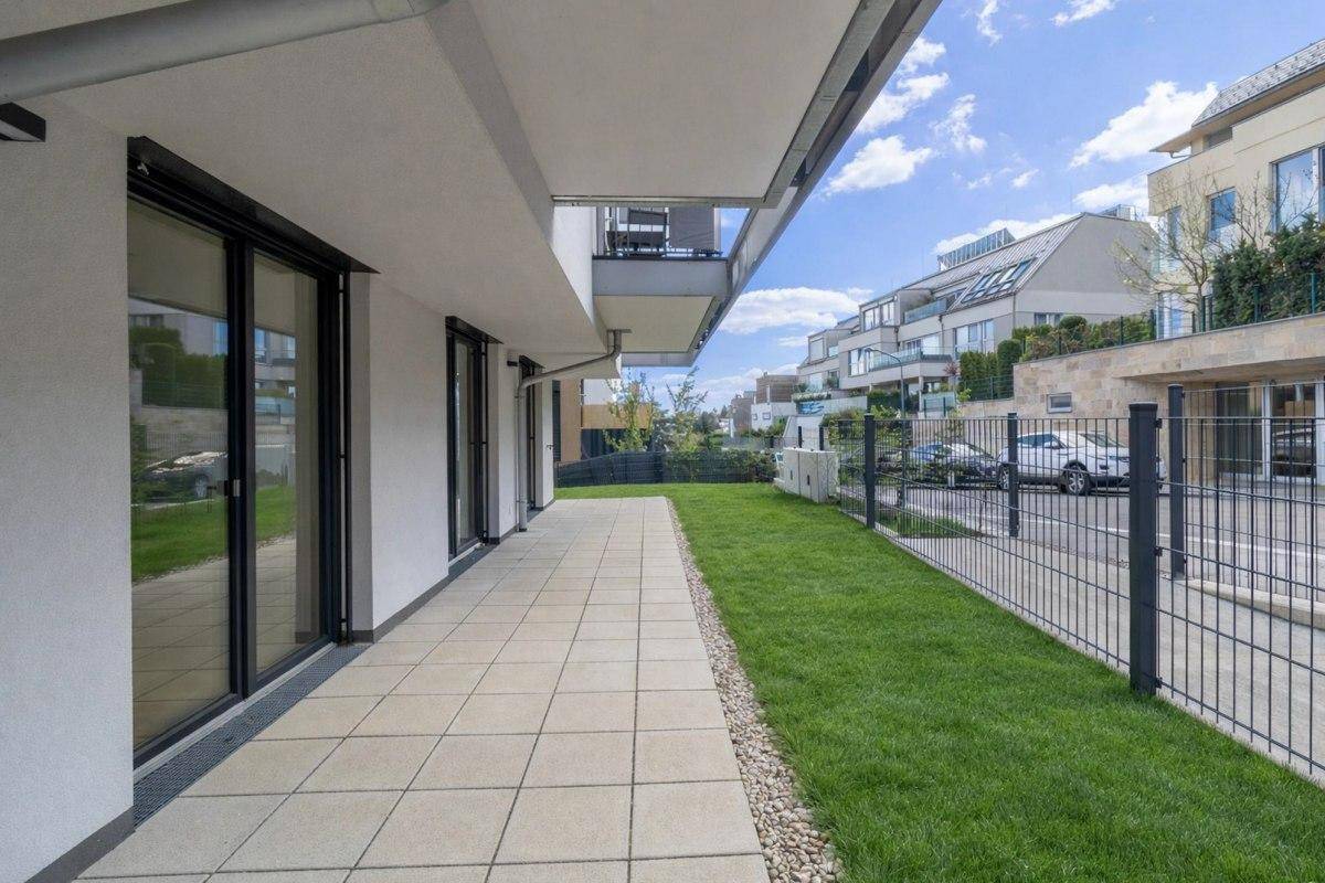 Lange gepflasterte Terrasse mit angrenzendem Rasen und einer hohen Hecke.