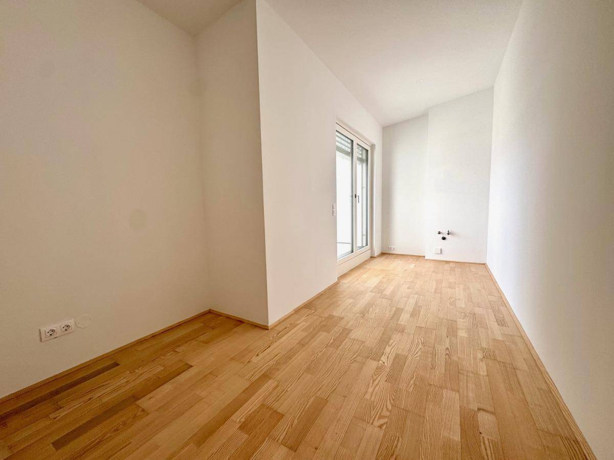 Helles Schlafzimmer mit Holzparkettboden und Zugang zu einer Terrasse durch eine große Schiebetür.