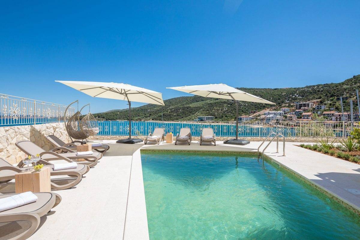 Sonniger Poolbereich mit bequemen Liegestühlen, Sonnenschirmen und weitem Meerblick.