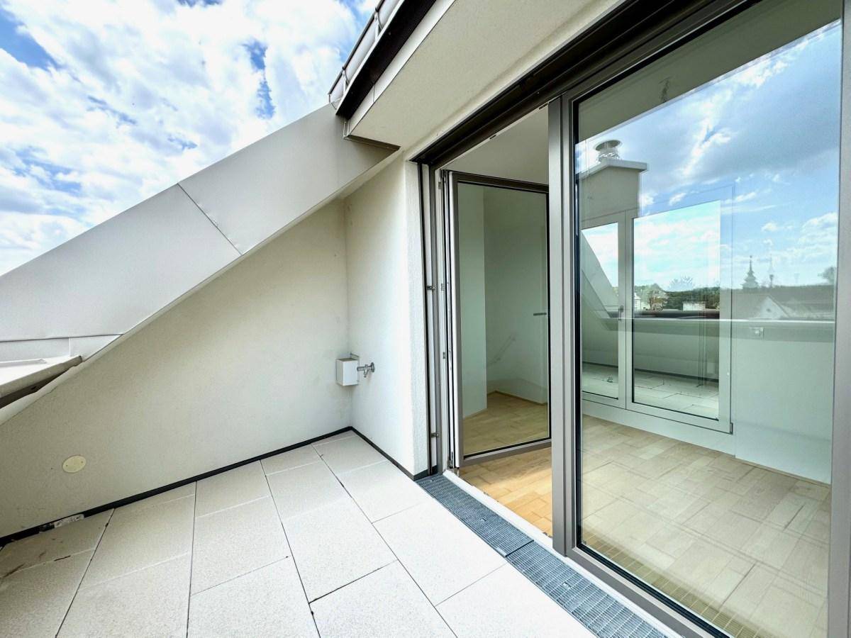 Heller Balkon mit Fliesenboden und großen Glasfenstern, die den Innenraum verbinden.