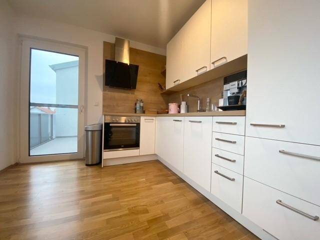 Moderne Einbauküche mit weißen Schränken, Holzakzenten und Zugang zu einem Balkon.