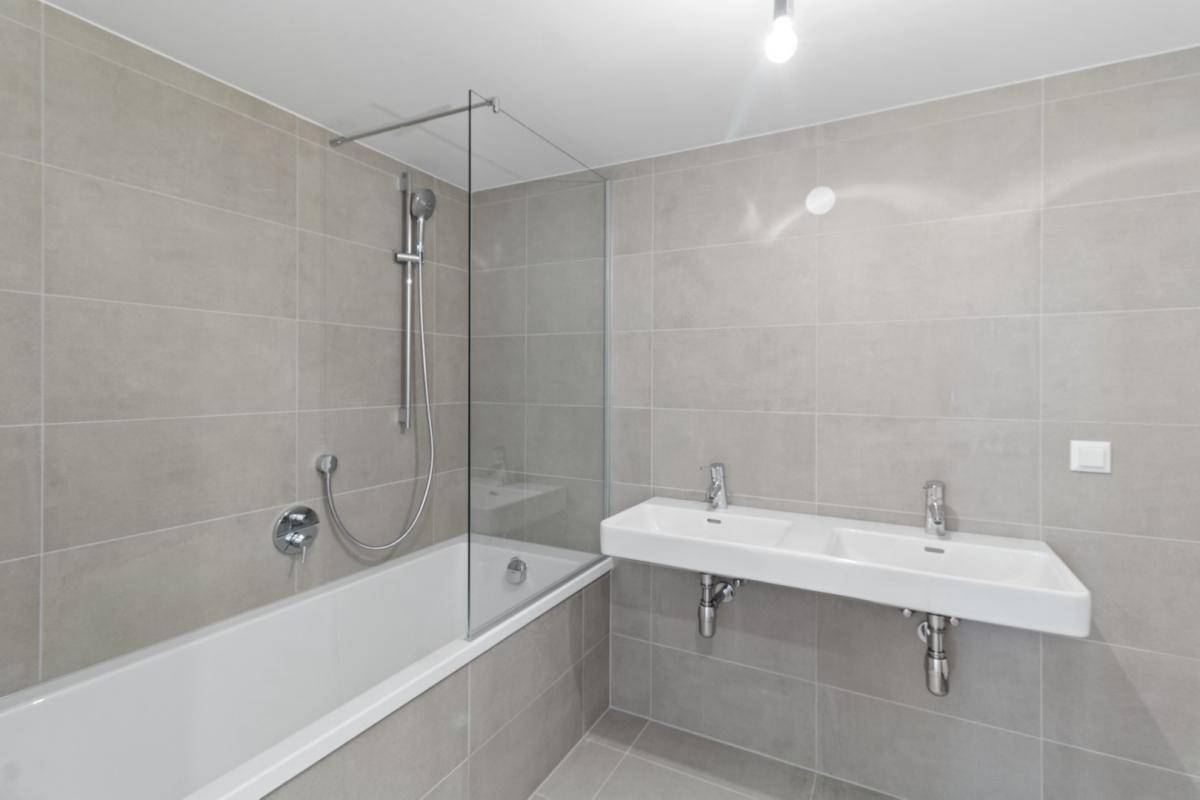 Modernes Badezimmer mit hellgrauen Fliesen, Badewanne und Doppelwaschbecken.