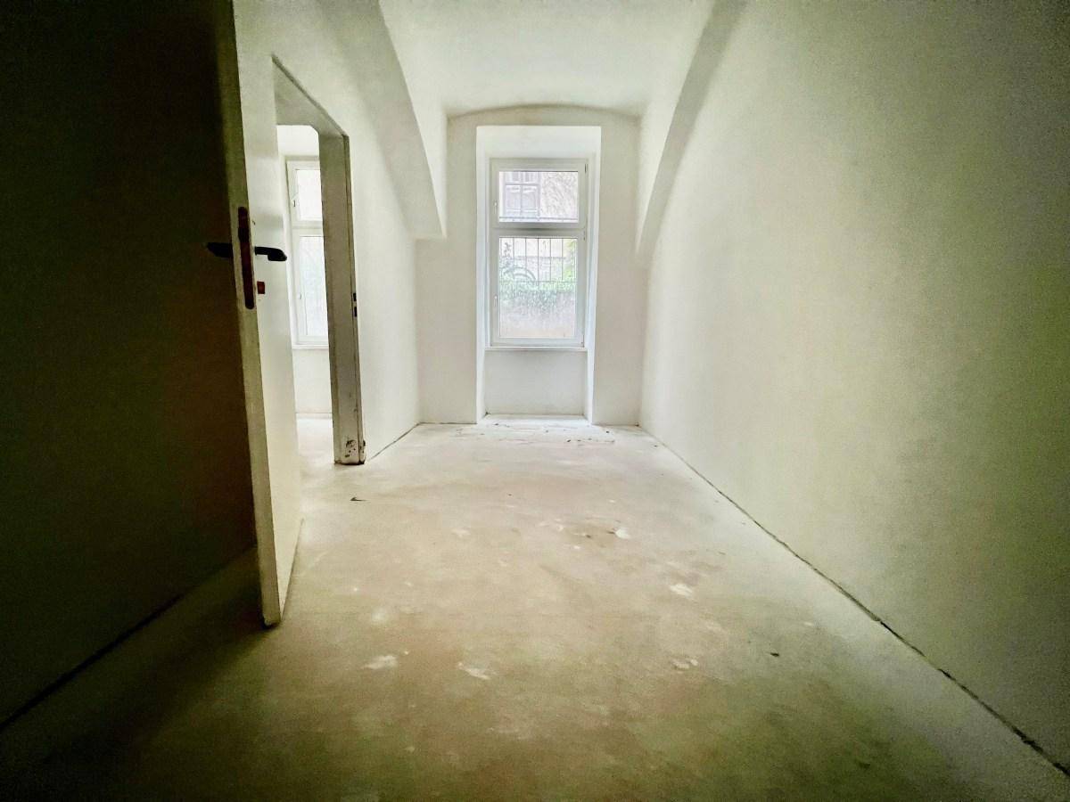 Unmöblierter Raum mit einem Fenster, unverputzten Wänden und Rohbetonboden, ideal für eine Renovierung.