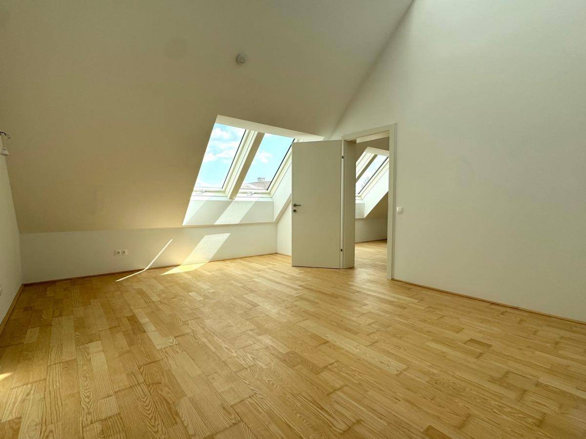 Heller Wohnraum mit schrägen Wänden, Holzparkett und mehreren Dachfenstern, die den Raum mit Licht füllen.