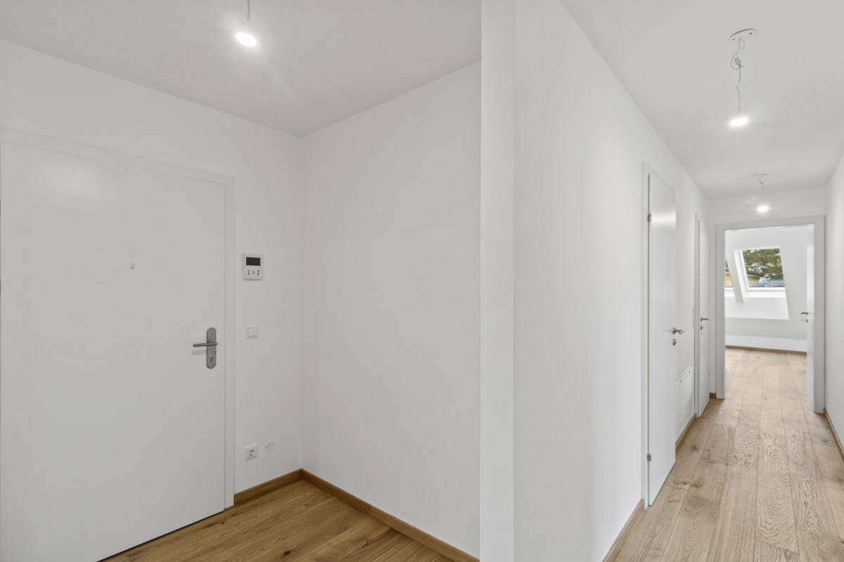 Heller Flur mit Holzboden und weißen Wänden, der zu weiteren Räumen im Dachgeschoss führt.